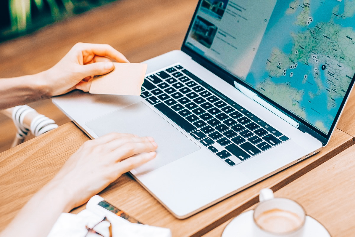 The Top Travel Scams to Avoid in 2025 (And How to Outsmart Them): A woman holding a credit card about to book her hotel booking in front of her laptop.