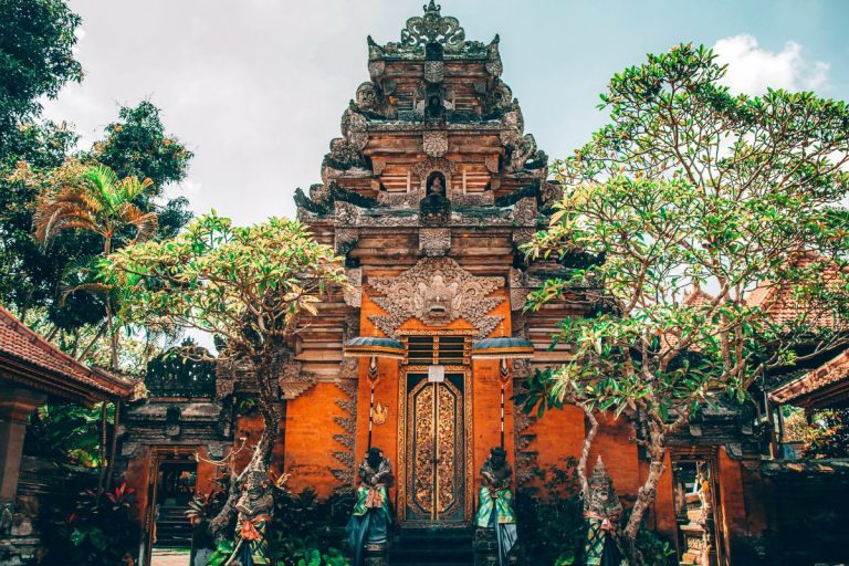 Balinese temple entrance in Ubud with intricate stone carvings, golden doors, guardian statues, and tropical trees, showcasing the cultural beauty of top Attractions in Ubud.