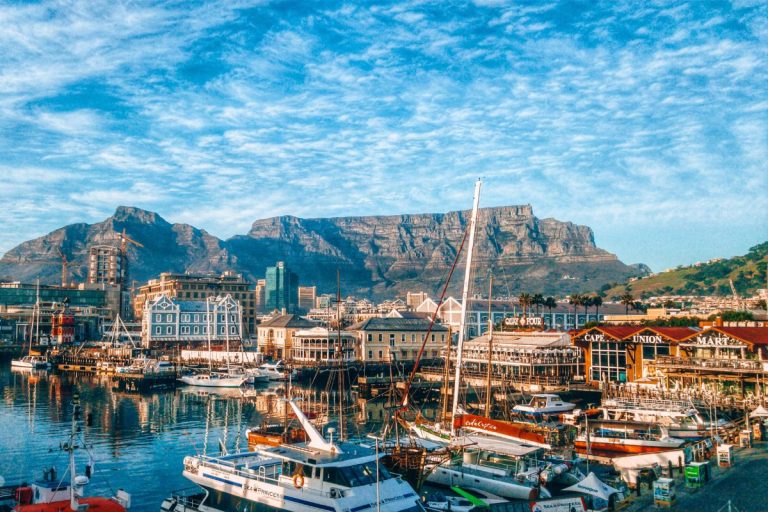 Colorful boats docked at Cape Town’s V&A Waterfront with Table Mountain rising in the background under a bright blue sky, a perfect view for the ultimate Cape Town travel guide.