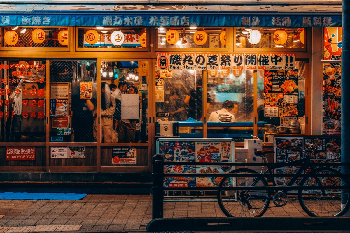 Japanese restaurant in Tokyo with colorful posters, hanging lanterns, and people dining inside, captured at night for a Tokyo Food Guide.